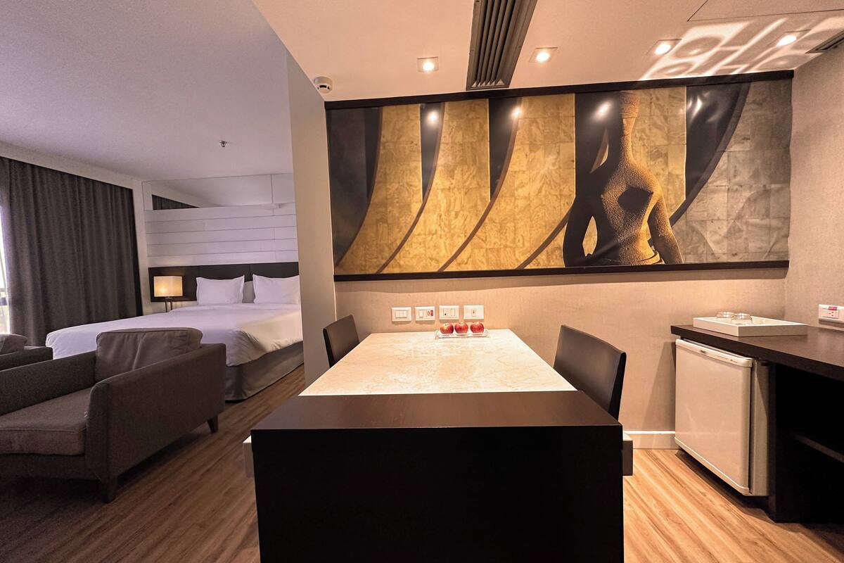 Una habitación de hotel moderna con cama, zona de estar, mesa de comedor y cocina.