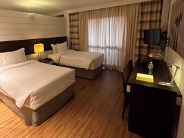 A hotel room with two beds, a desk, a chair, a TV, and a window with curtains.