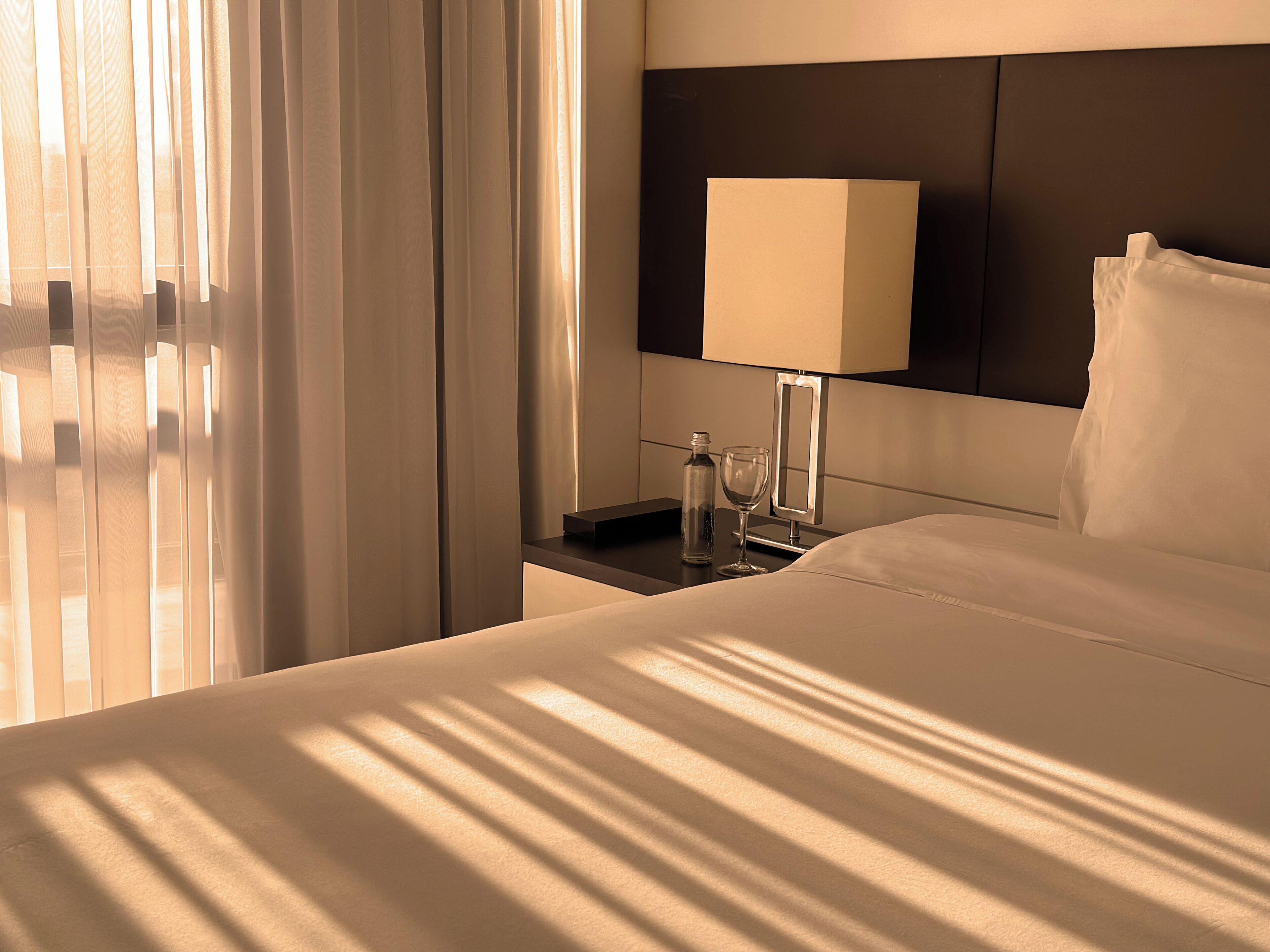 Una habitación de hotel con cama, una mesita de noche con lámpara, un vaso de agua y una botella.