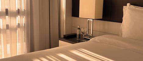 Una habitación de hotel con cama, una mesita de noche con lámpara, un vaso de agua y una botella.