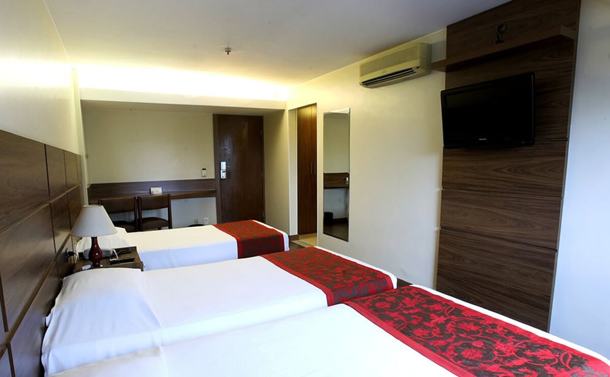 Quarto de hotel com duas camas, uma escrivaninha, uma cadeira, uma TV e um espelho.