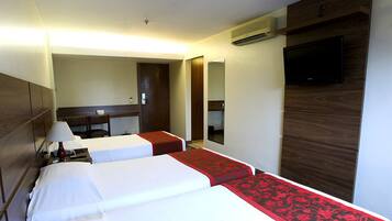 Quarto de hotel com duas camas, uma escrivaninha, uma cadeira, uma TV e um espelho.