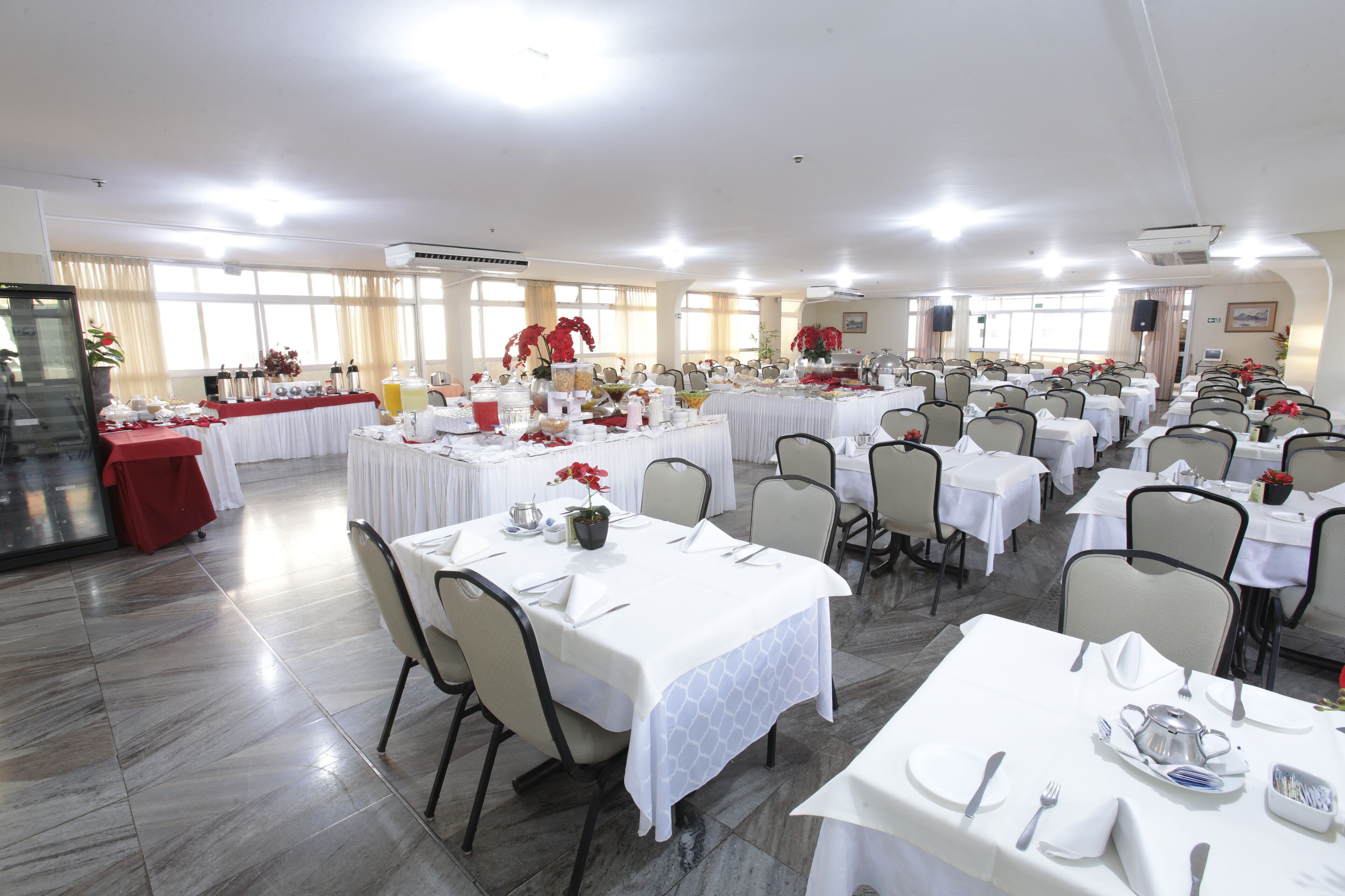 A banquet hall with multiple round tables set for dining, each with white tablecloths and silverware.