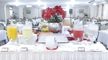 A buffet setup with various food and drink options, including fruit juices and a central floral arrangement.