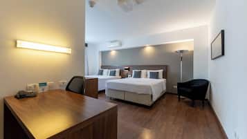 A hotel room with a wooden desk, two beds, a chair, and a standing lamp.