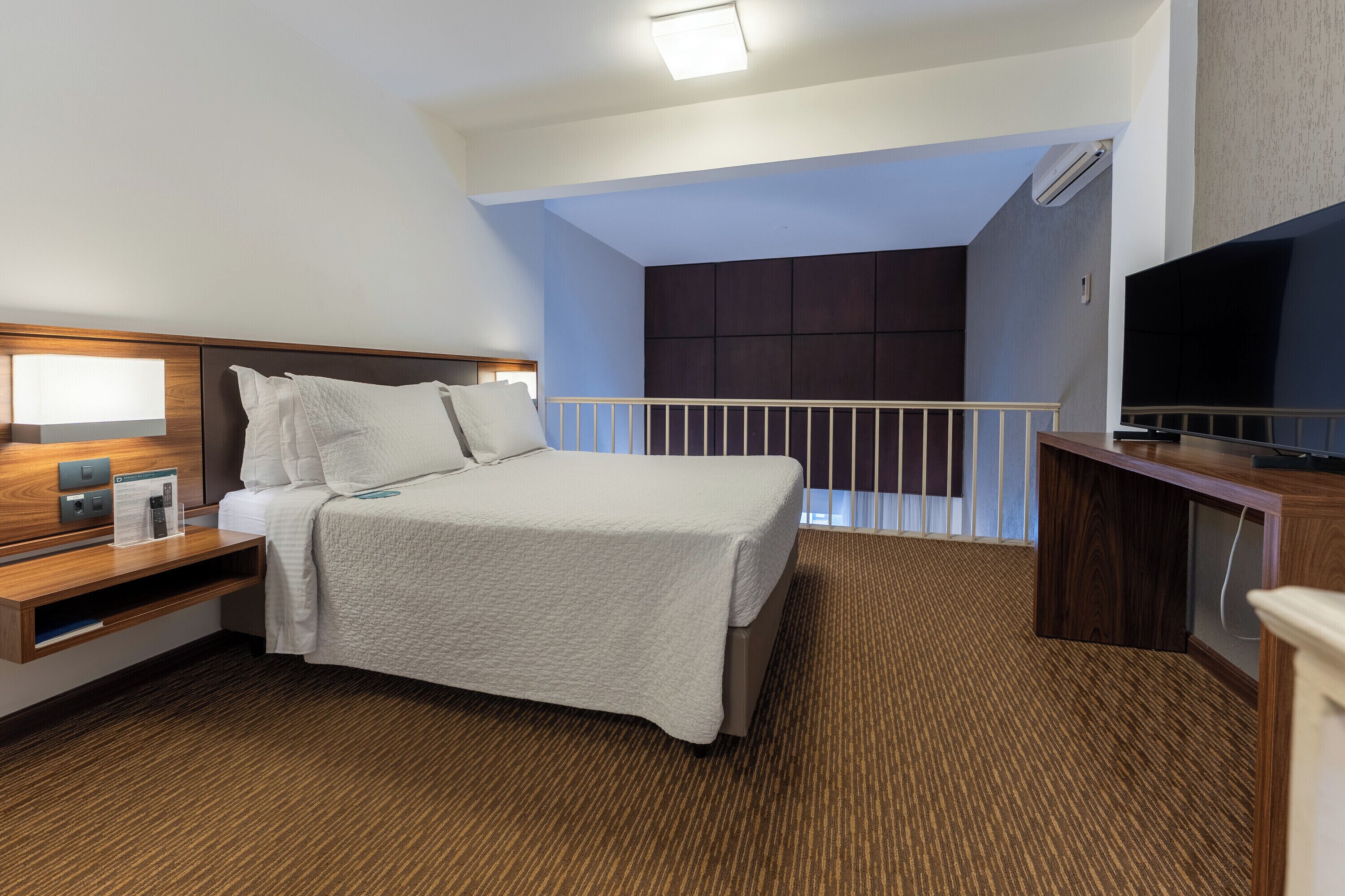 Habitación de hotel con cama, mesita de noche, televisión y balcón con vistas.