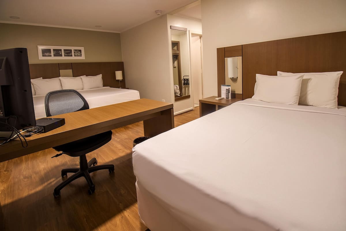 A hotel room with a large bed, a desk with a chair, a TV, and a mirror.