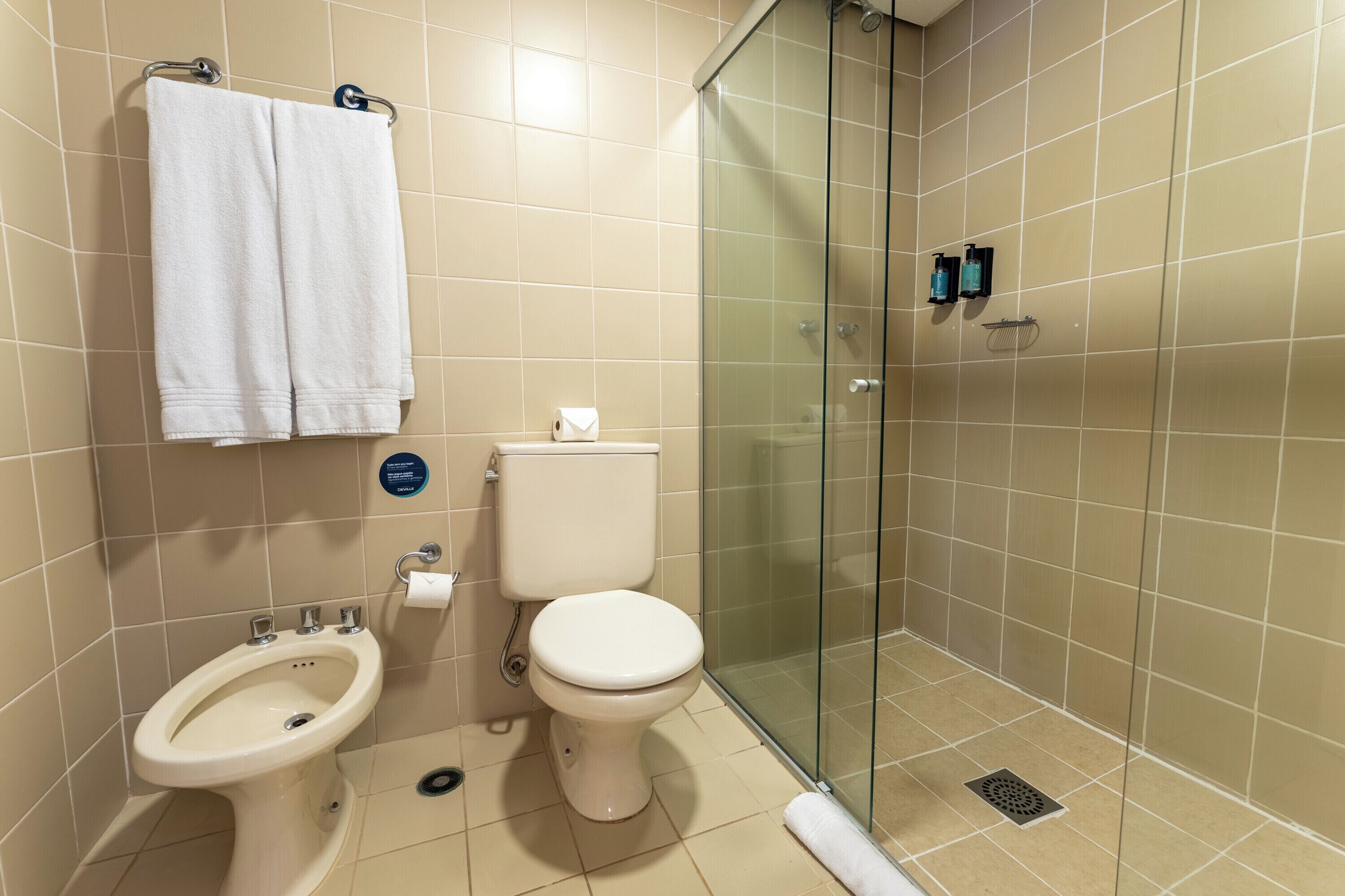 A bathroom with a toilet, bidet, and glass-enclosed shower stall.
