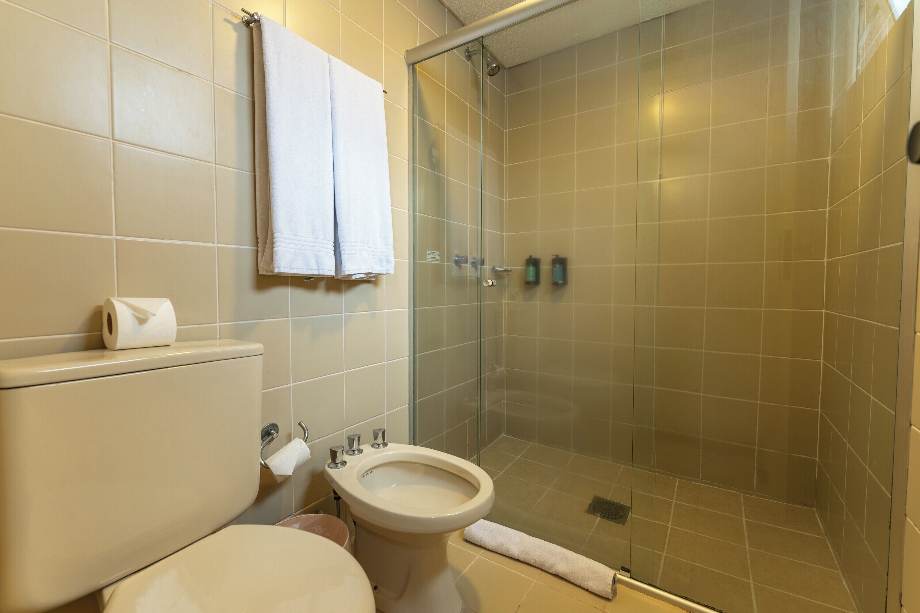 Een badkamer met toilet, bidet en douchecabine met glazen wanden.