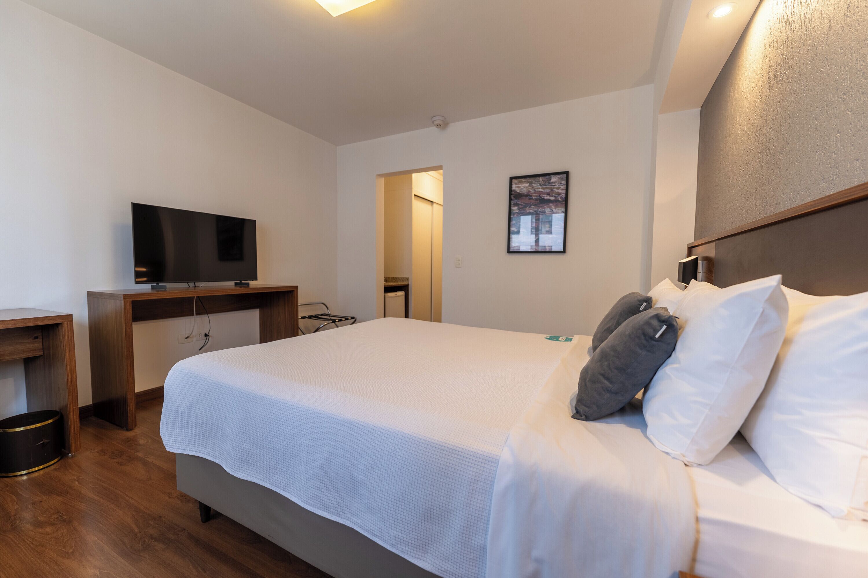 A hotel room with a bed, a television, a desk, and a painting on the wall.