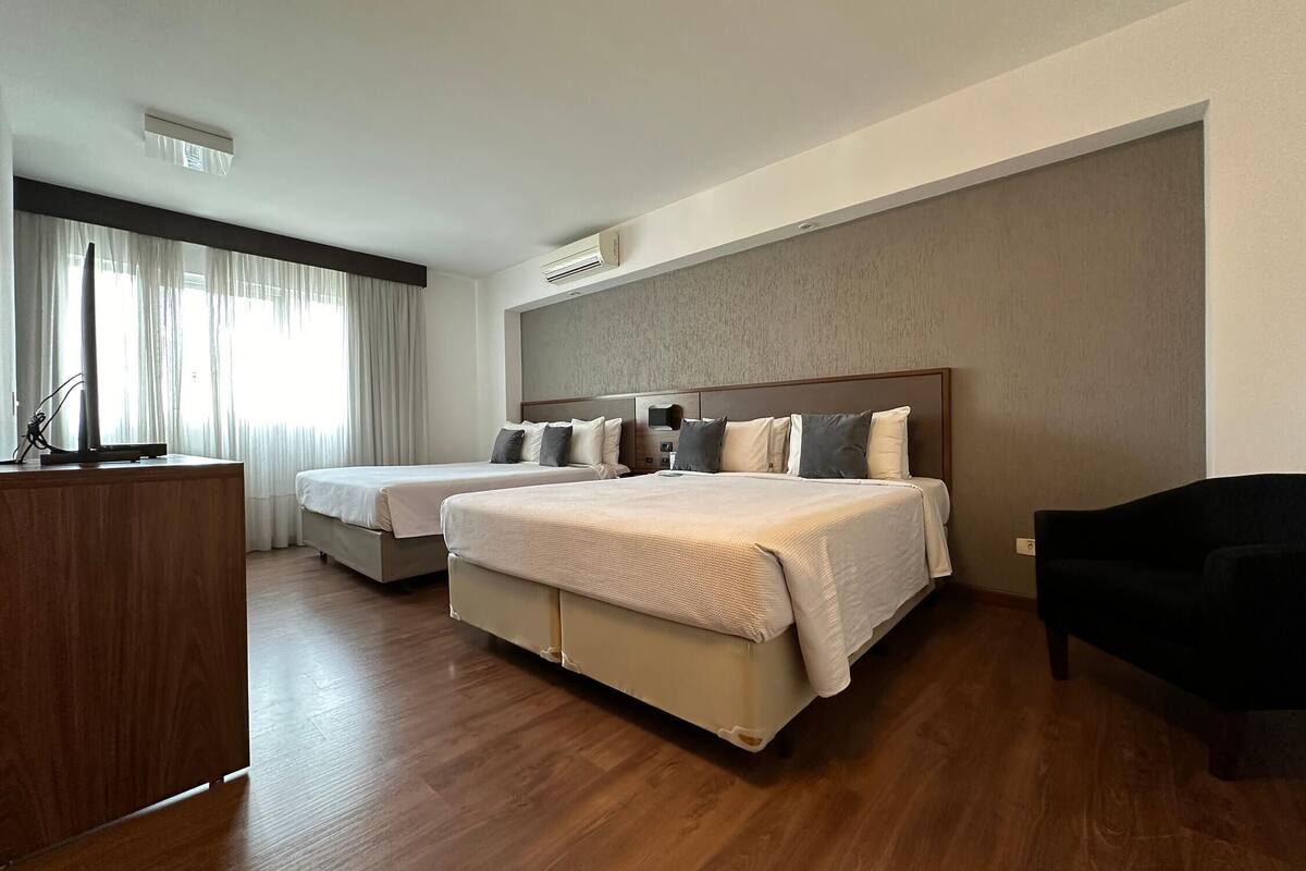 A hotel room with two beds, a desk, and a black chair.