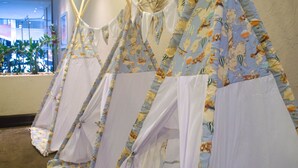 A row of teepees with floral patterns and white fabric, set against a wall with a window view. - Hotel Deville Curitiba (Curitiba)