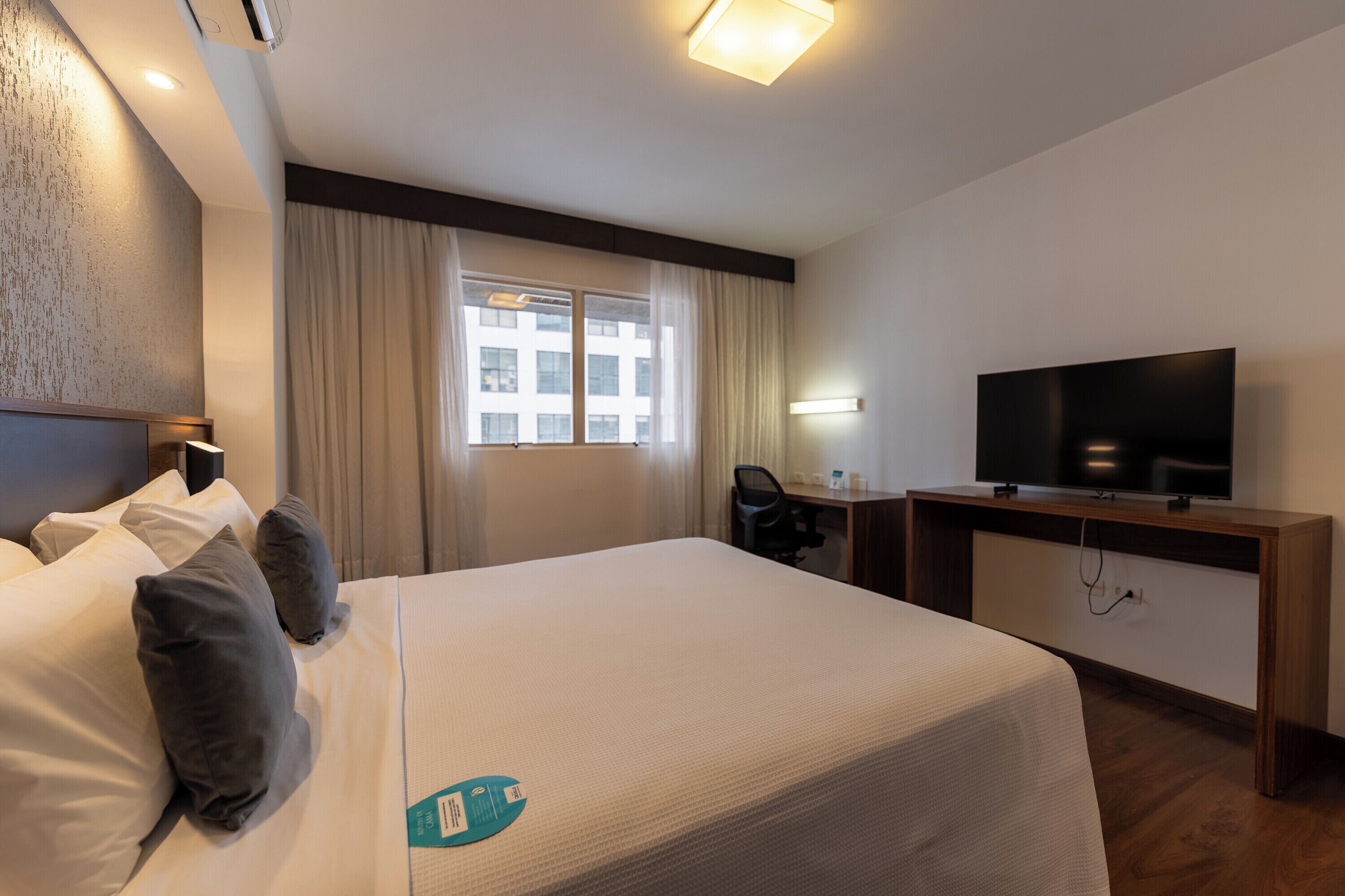 A hotel room with a bed, a desk, a chair, a television, and a window with curtains.