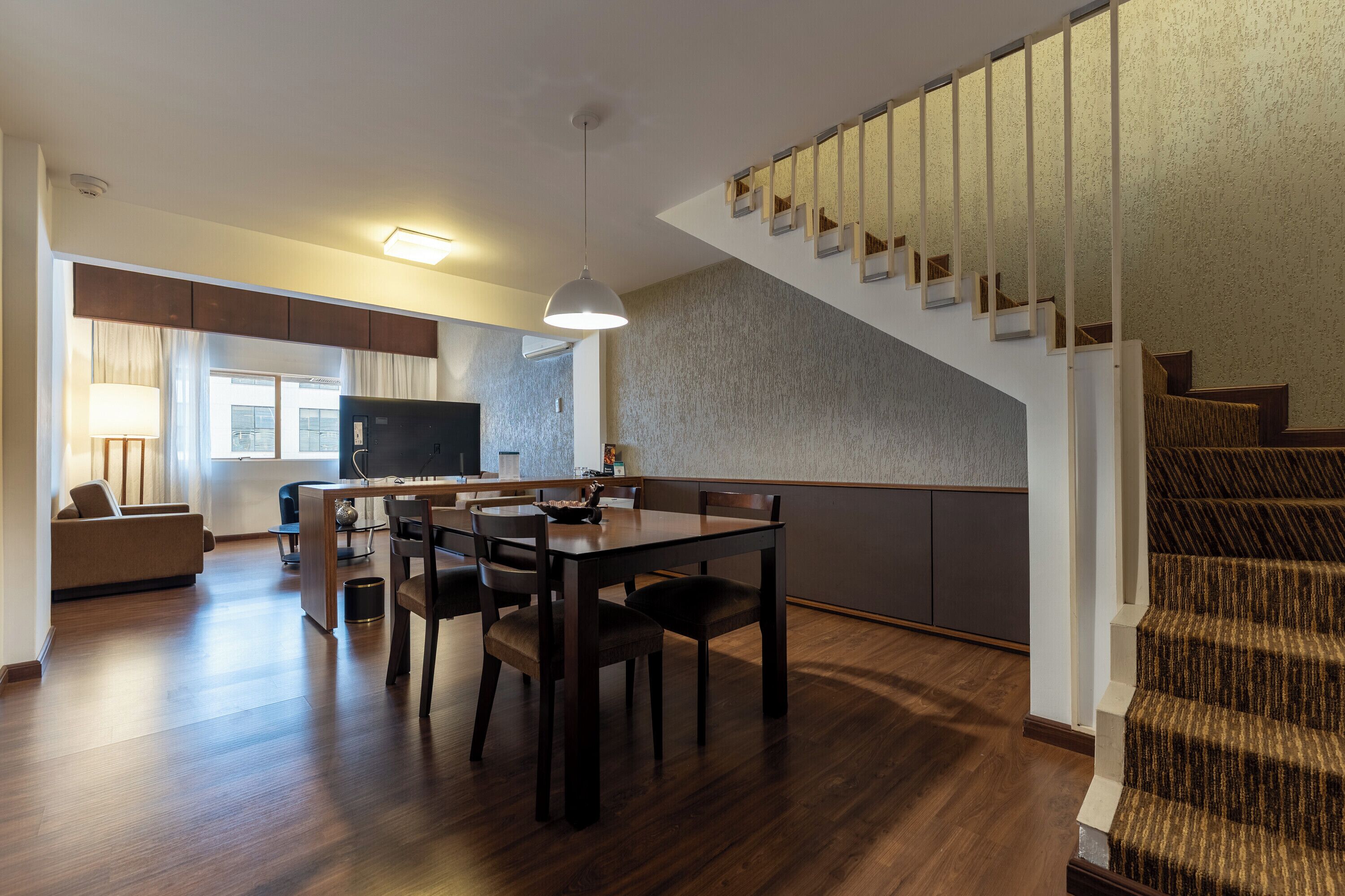 A modern living room with a dining area, a staircase, and a kitchen in the background.