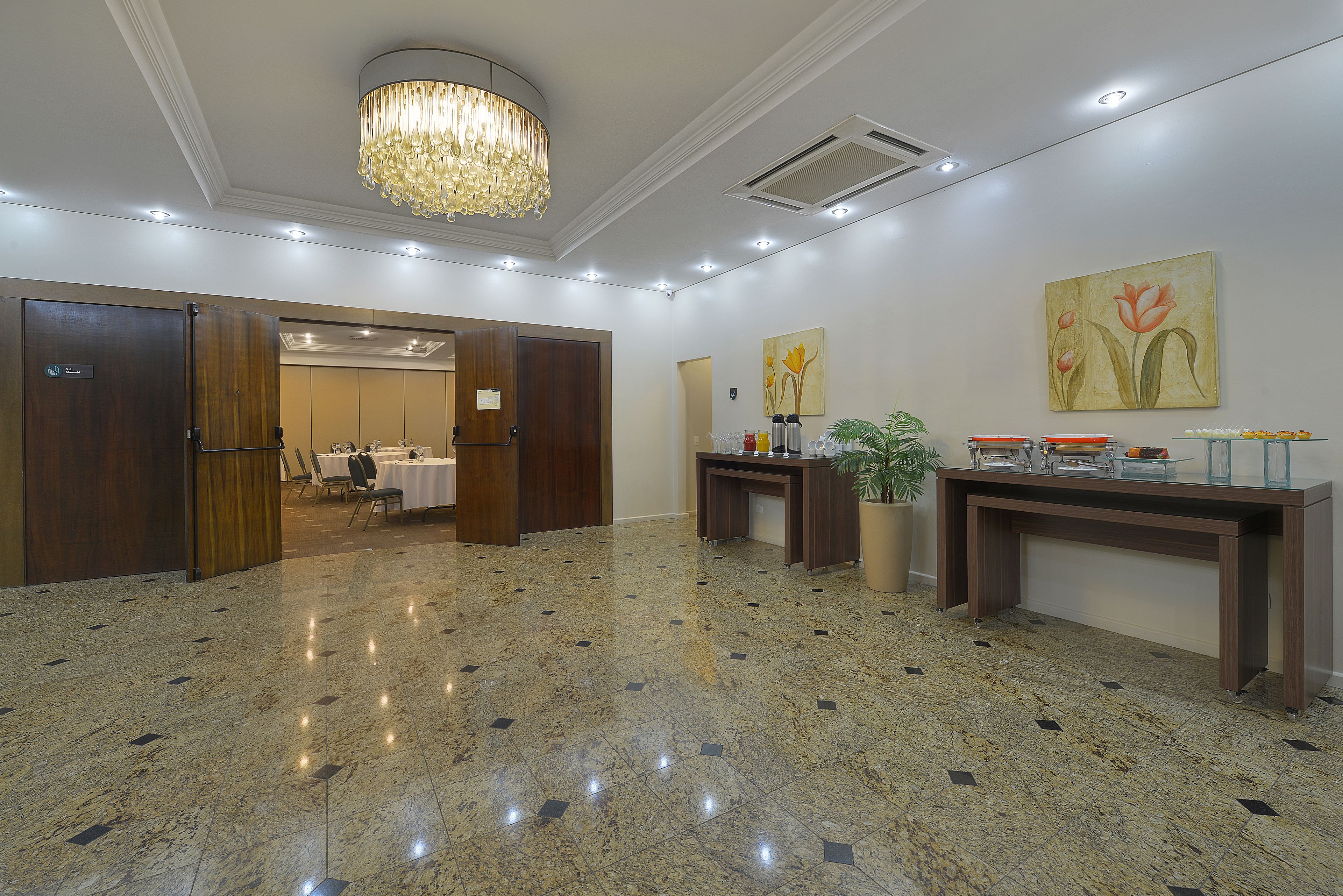 A spacious lobby with a polished marble floor, a chandelier, and a reception desk with a plant.