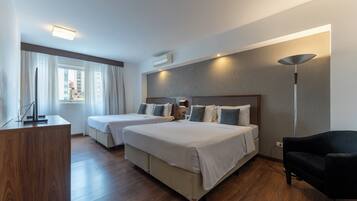 A hotel room with two beds, a desk, a chair, and a large window with curtains.