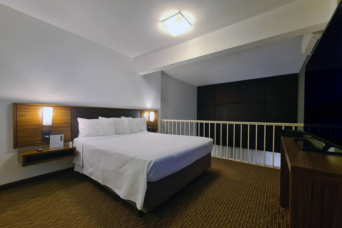 A hotel room with a large bed, bedside tables, a desk, and a balcony with a railing.