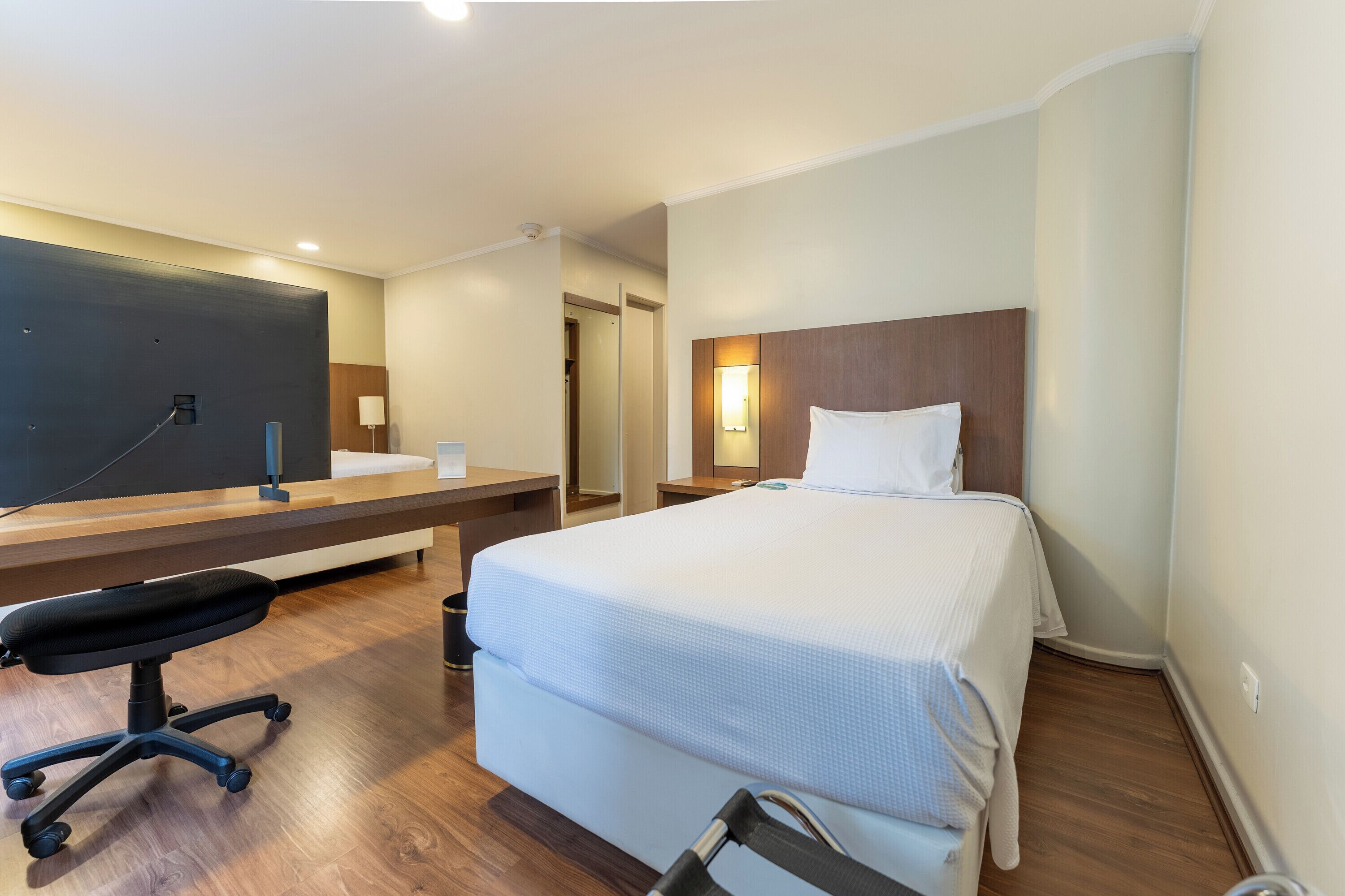 Ein Hotelzimmer mit Bett, Schreibtisch, Stuhl, Spiegel und Nachttisch.