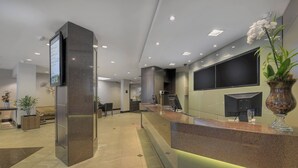 A modern reception area with a marble counter, a large digital screen, and a potted orchid. - Hotel Deville Curitiba (Curitiba)