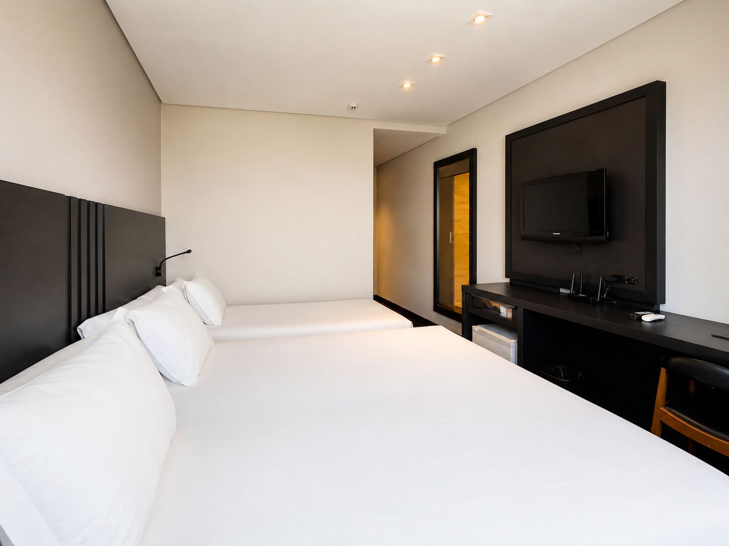 A hotel room with two beds, a desk, a TV, and a mirror.