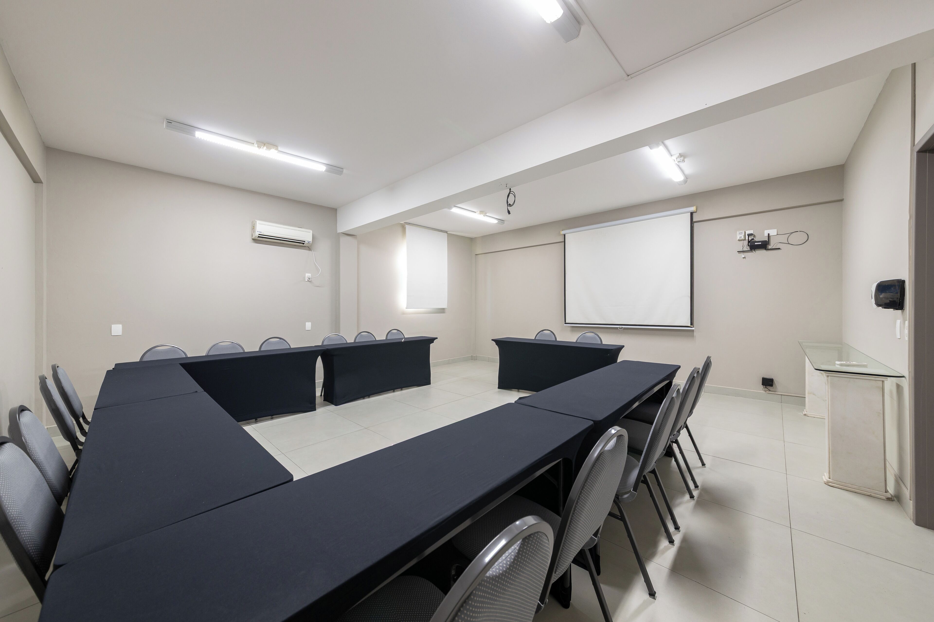 Un salón de conferencias con una larga mesa, sillas, una pantalla de proyector y una pizarra.