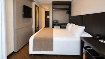 A hotel room with a bed, bedside table, TV, and a desk with a phone.
