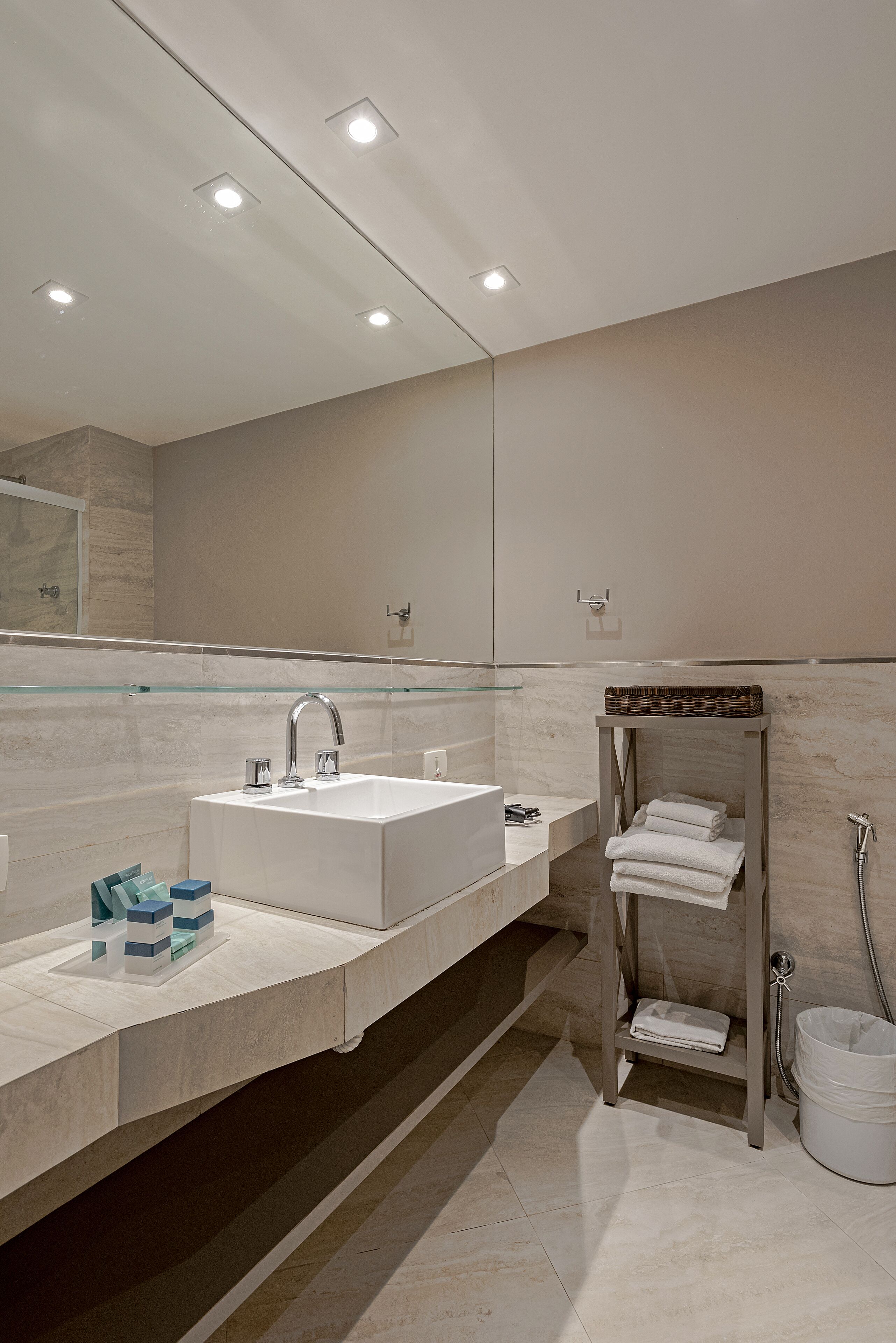 A modern bathroom with a large mirror, a white sink, and a glass shelf.