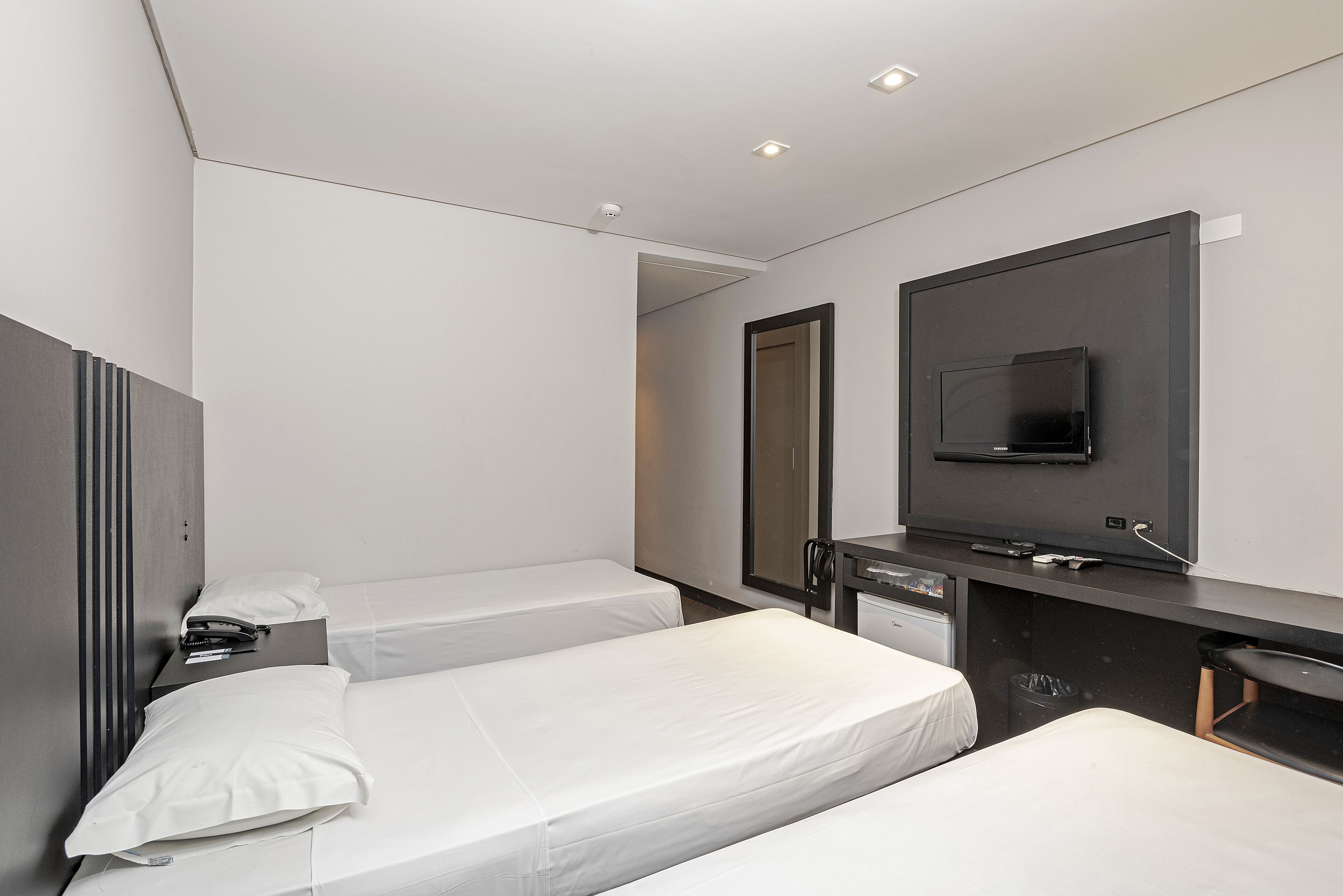 A hotel room with two single beds, a desk with a flat-screen TV, a mirror, and a small trash bin.