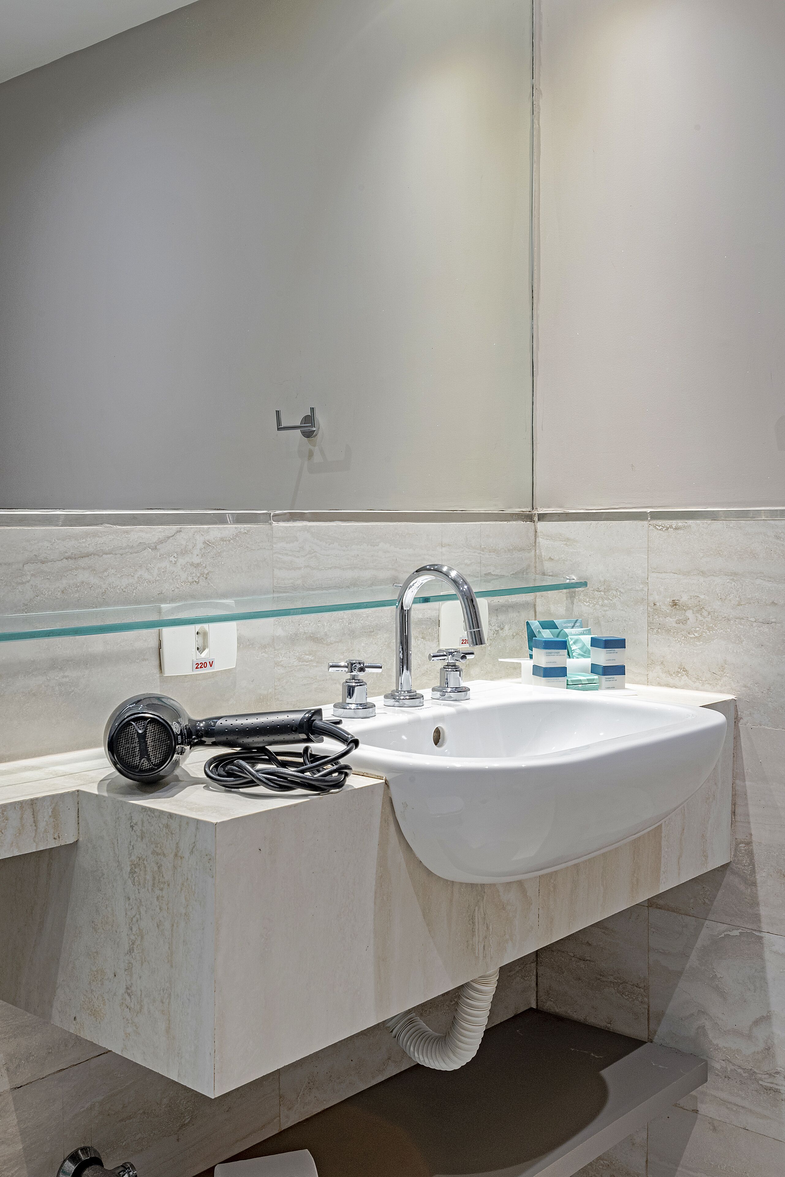 Un baño moderno con un lavamanos blanco, un estante de vidrio y un secador de pelo.
