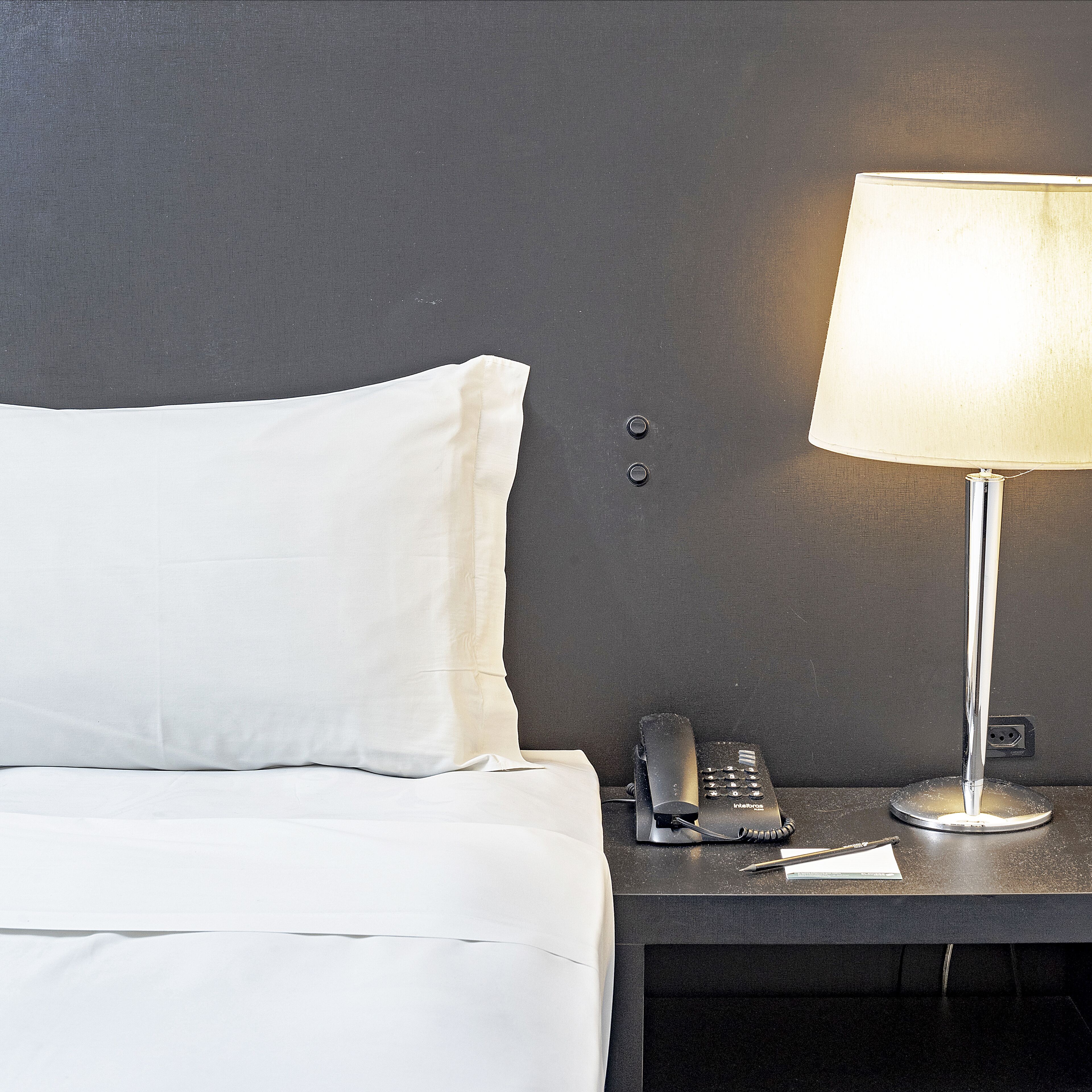 A neatly made bed with white bedding, a bedside table with a lamp, and a telephone.