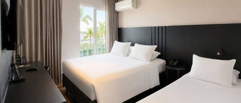 A hotel room with two beds, a desk with a TV, and an air conditioning unit.
