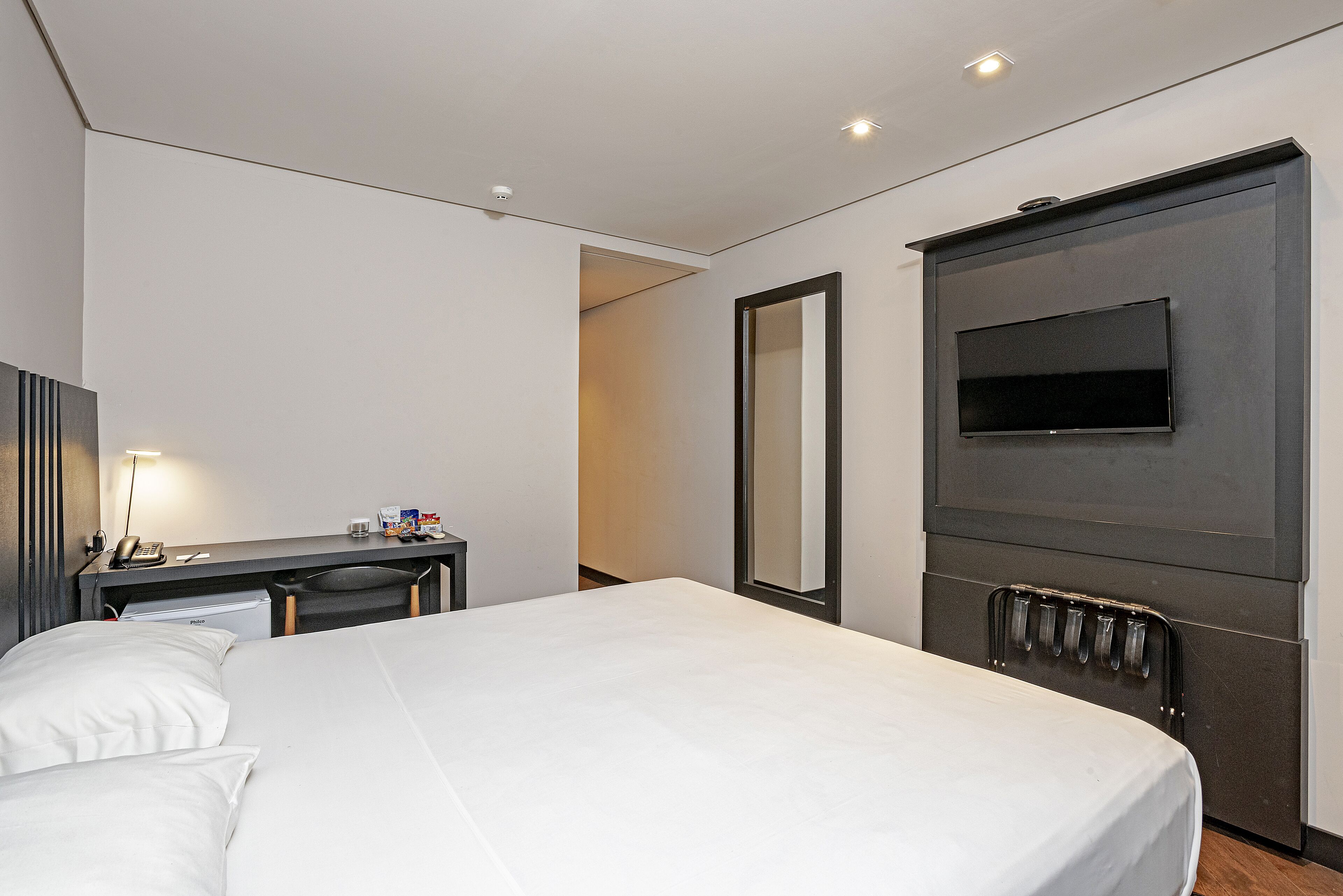 A hotel room with a bed, a desk, a chair, a TV, and a mirror.