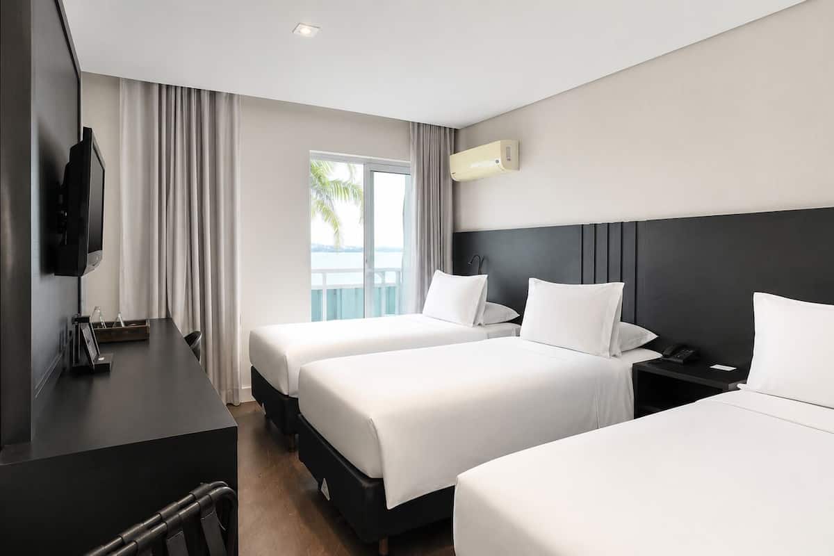 Ett hotellrum med två sängar, ett skrivbord, en TV och ett fönster med gardiner.