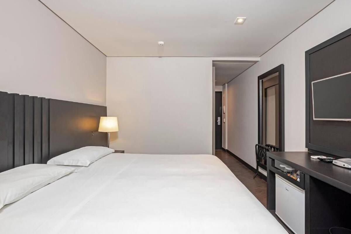 Ett hotellrum med en säng, ett skrivbord med en dator, en tv och en lampa.