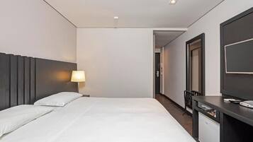 Una habitación de hotel con una cama, un escritorio con una computadora, un televisor y una lámpara.