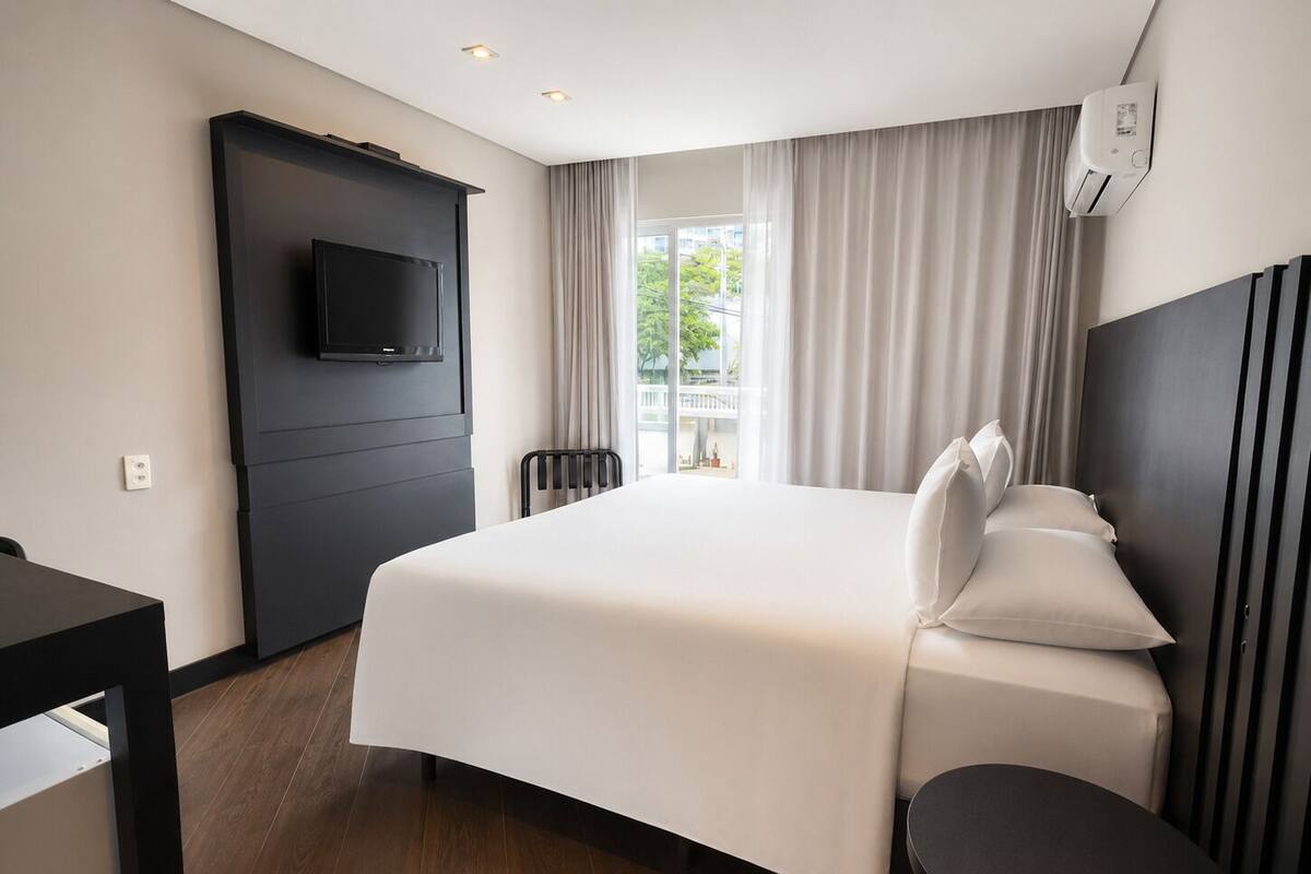 Ett hotellrum med en säng, en tv som är monterad på väggen, ett skrivbord och en stol.