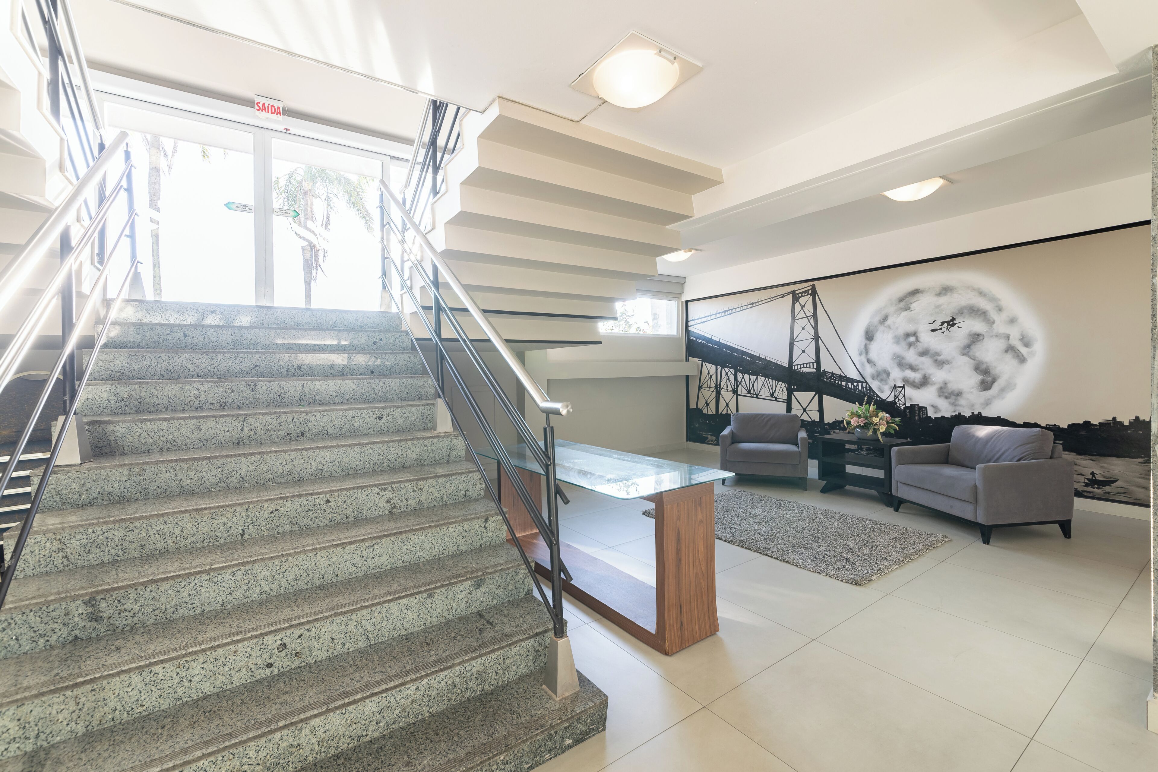 Un escalier menant à un palier où se trouvent une table basse en verre et deux canapés.
