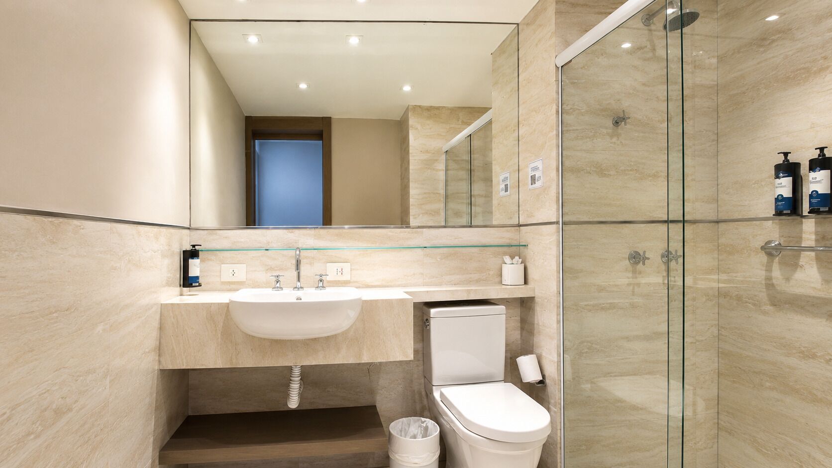 A modern bathroom with a glass shower enclosure, a sink with a glass shelf, and a toilet.