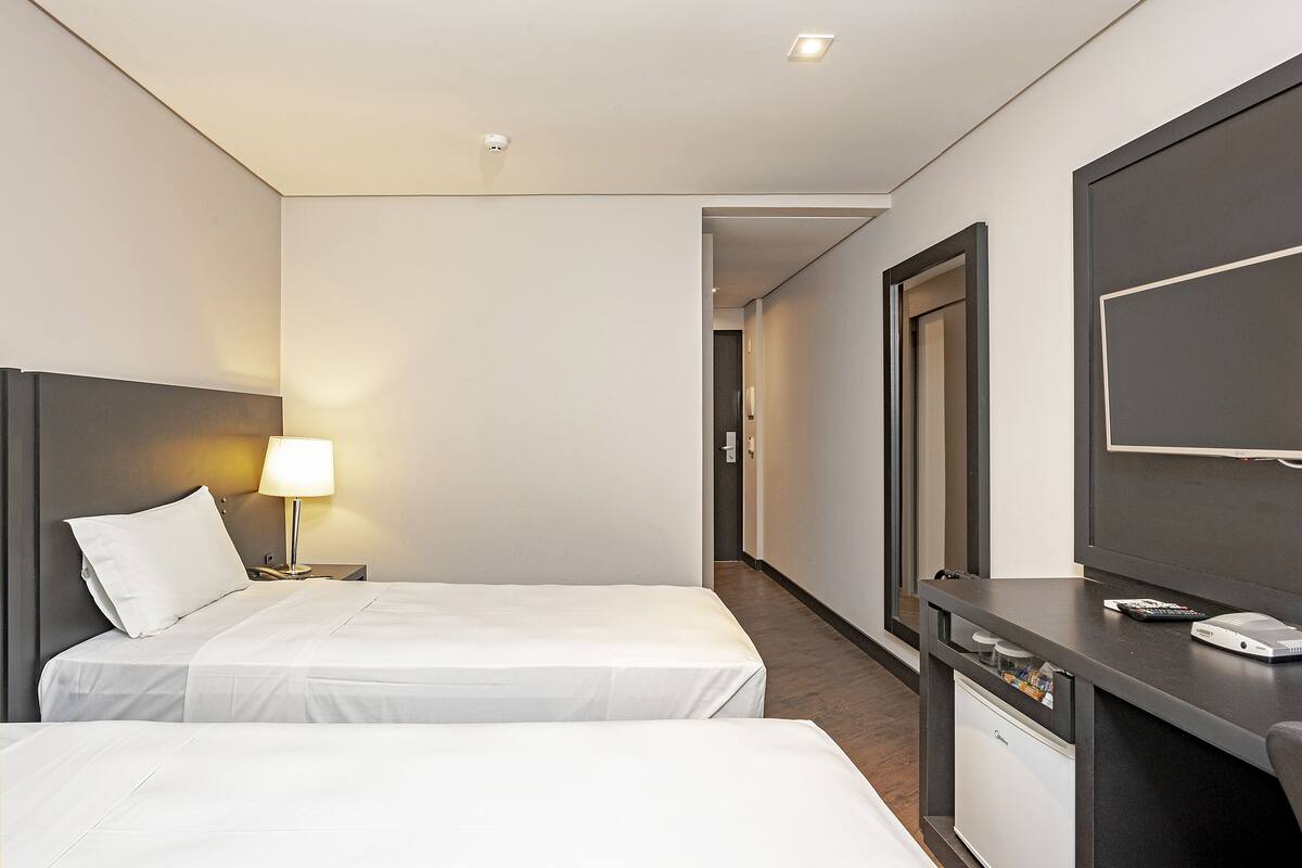 Ett hotellrum med två sängar, ett skrivbord med en dator, en lampa och en tv.