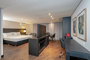 Una camera d'albergo con un letto, una scrivania, una televisione e opere d'arte appese al muro.