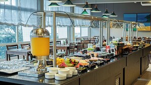 A buffet setup with various food items, a juice dispenser, and a seating area with tables and chairs. - Slaviero Baía Norte Florianópolis (Florianópolis)