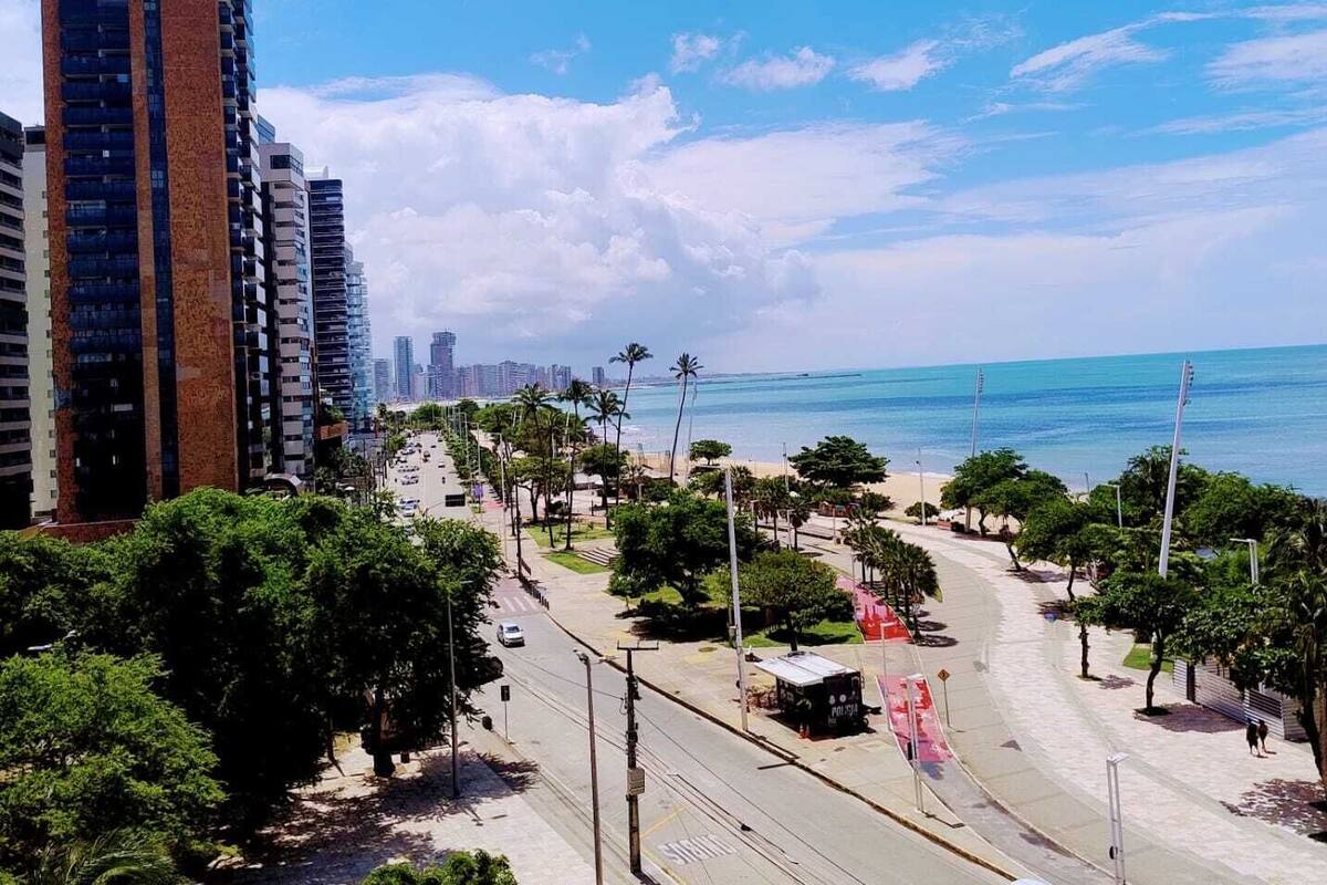 A coastal cityscape with modern high-rise buildings, a wide road, and a beach in the background.