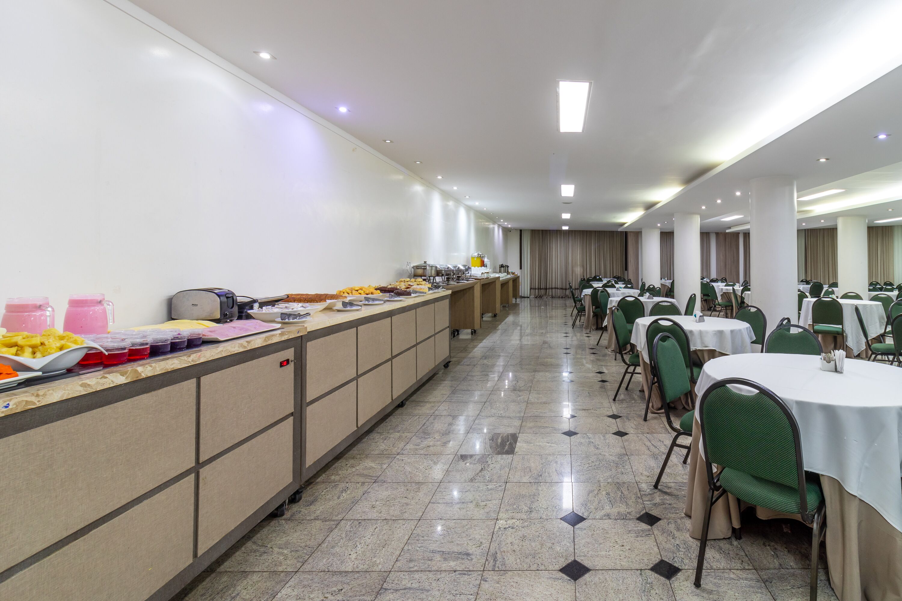 A long buffet line with various food items and a counter with drinks.