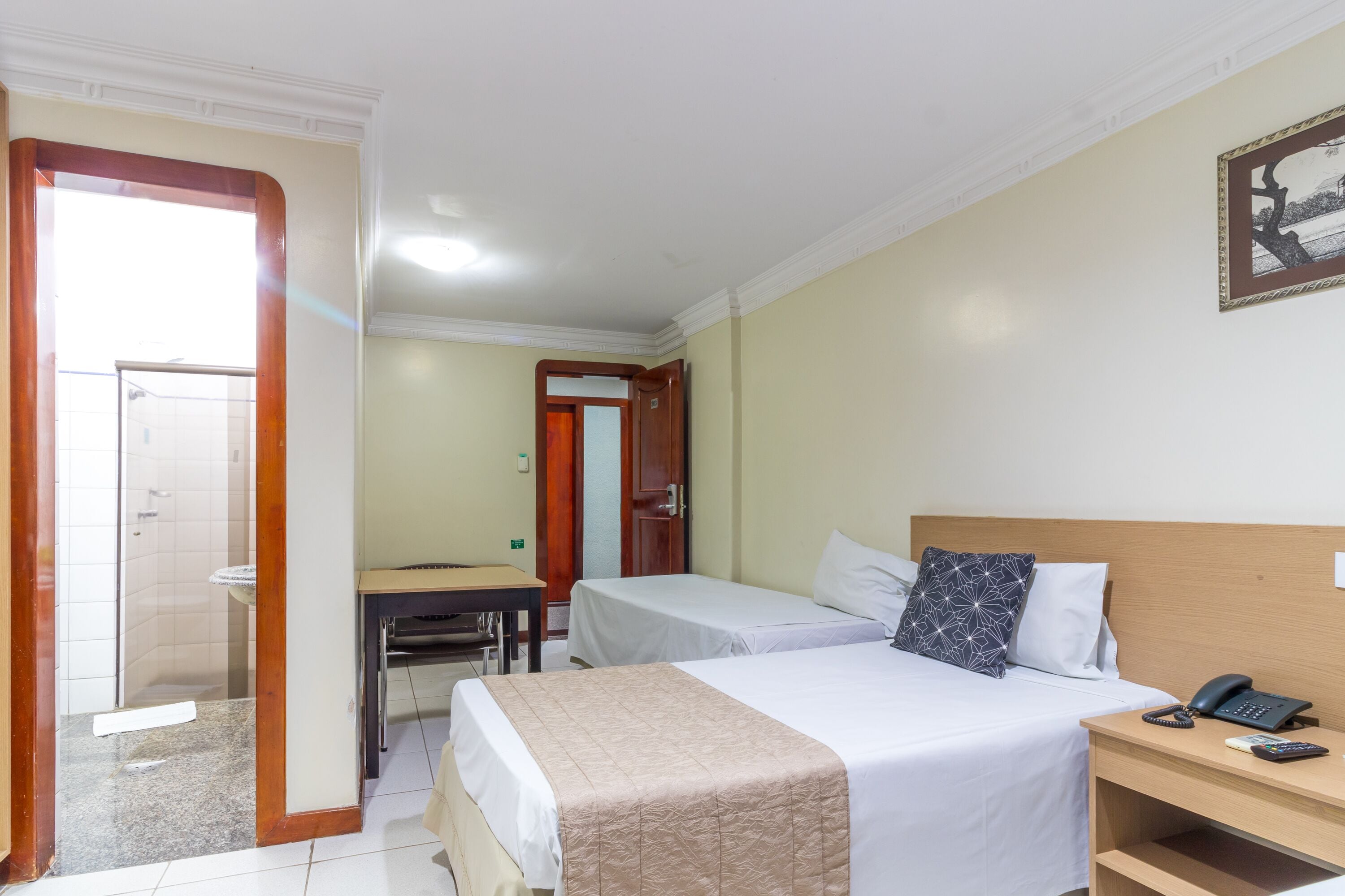 Habitación de hotel con dos camas, un escritorio y un baño visible a través de una puerta abierta.