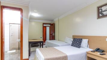 Habitación de hotel con dos camas, un escritorio y un baño visible a través de una puerta abierta.