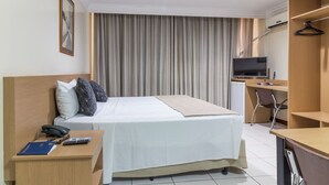 Una habitación de hotel con cama, mesita de noche, escritorio, silla, televisor y armario.