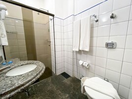 Un baño con lavamanos de granito, azulejos blancos, cabina de ducha de vidrio y un inodoro con toalla.