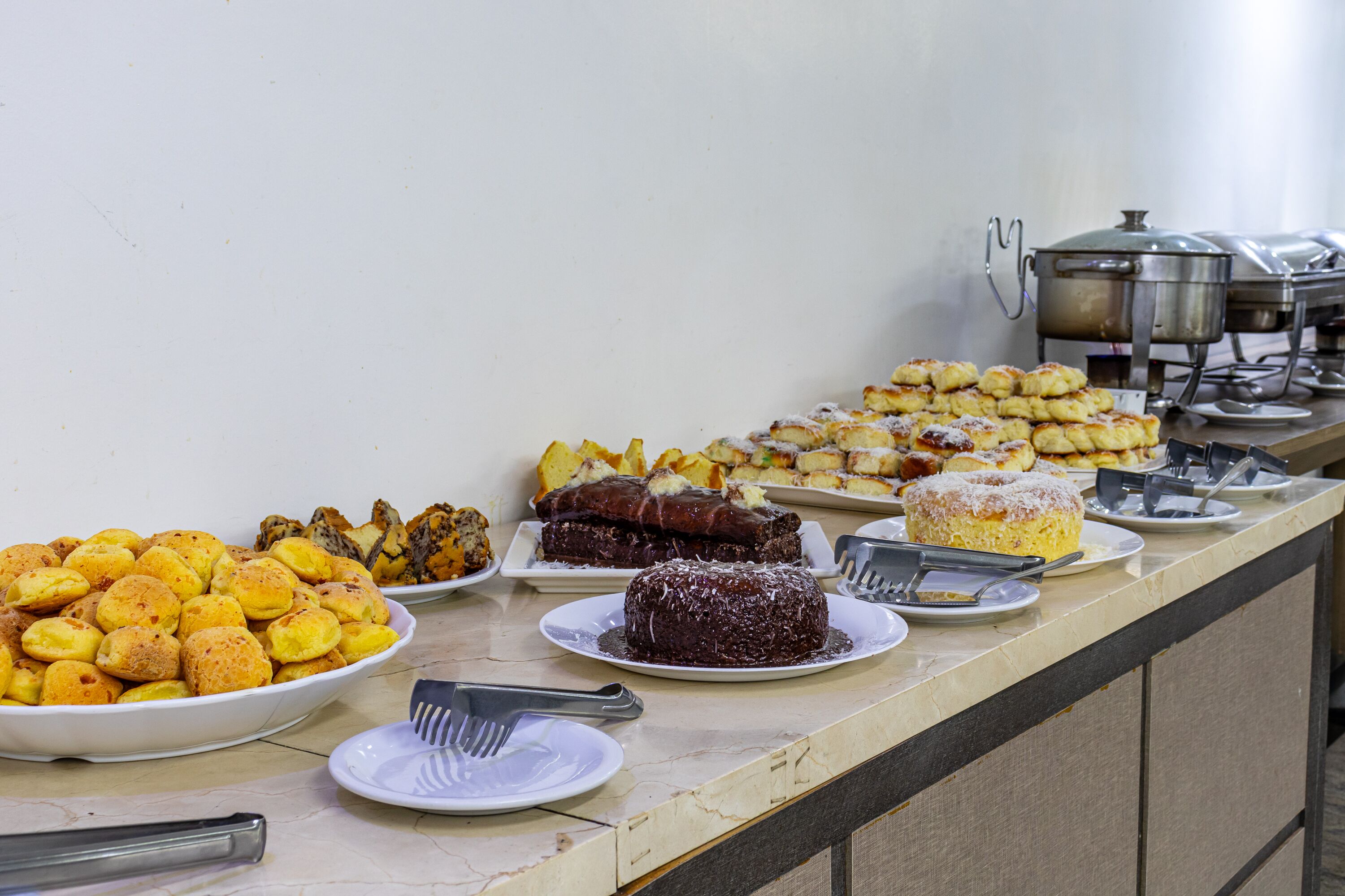 Buffet com diversos pratos, incluindo pão, doces e sobremesas.