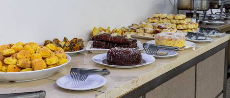 Un bufé con diversos platos que incluyen pan, bollería y postres.