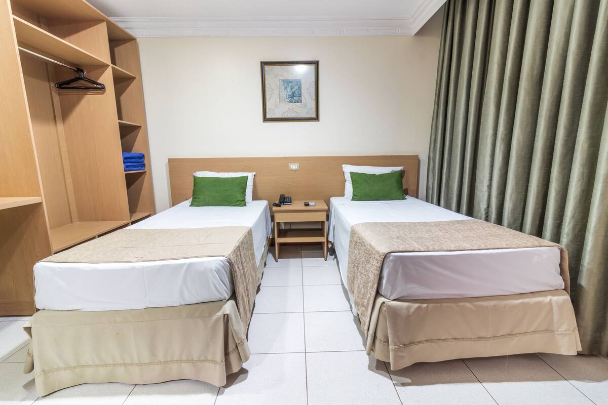 Ett hotellrum med två sängar, en garderob i trä, ett litet sängbord och en inramad tavla på väggen.